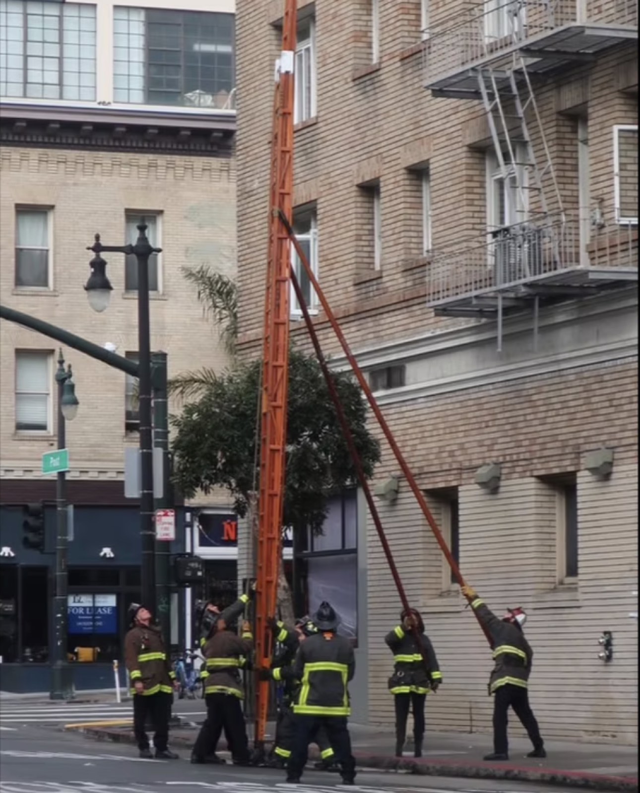 A crew raising a ground ladder to the upper floors of a city building
